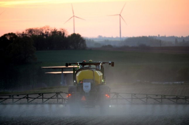 Un agriculteur français pulvérise un herbicide alors que des éoliennes marquent l'horizon.