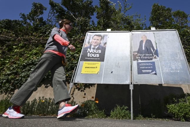 Un piéton passe devant des affiches de campagne du président français et candidat à la réélection du parti La République en Marche (LREM) Emmanuel Macron (G) et de la candidate à la présidence du parti d'extrême droite français Rassemblement National (RN) Marine Le Pen.