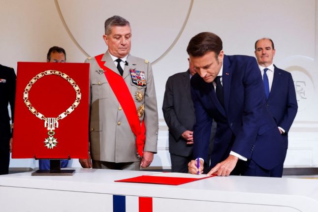 Le président français Emmanuel Macron (à droite) signe le protocole aux côtés de son grand chancelier le général Benoit Puga (à gauche) à l'Elysée