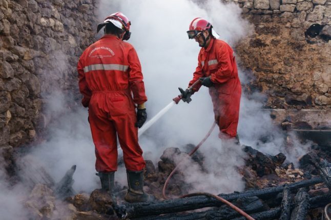 Des pompiers éteignent les décombres fumants d'une maison incendiée en Espagne.